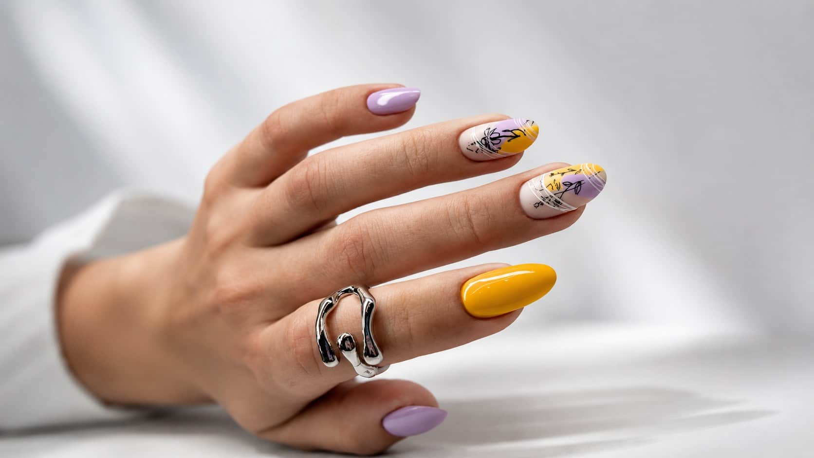 A hand with lilac and yellow floral nail art over a soft neutral base